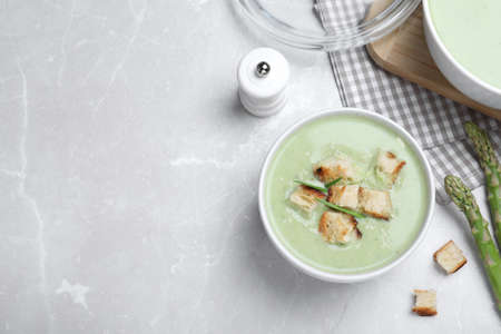 Bowl of delicious asparagus soup served on light gray table, flat lay. Space for textの写真素材