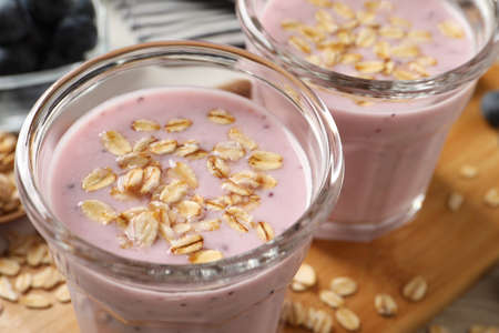 Glasses of tasty blueberry smoothie with oatmeal on wooden board, closeup