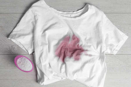 White t-shirt with stained and powdered detergent on wooden surface, flat lay. hand washing laundry