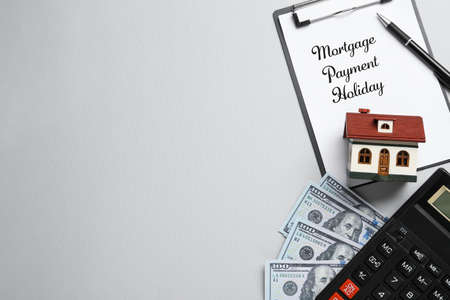Clipboard with words Mortgage Payment Holiday, house model, calculator and money on gray background, flat lay. Space for textの写真素材