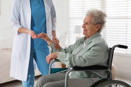 Caregiver assisting senior woman in wheelchair indoors. home health care service