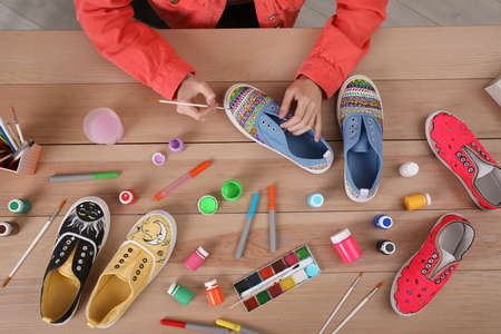 Woman painting on sneaker at wooden table, top view. custom shoes