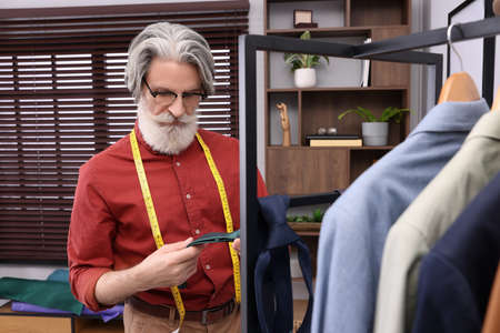 Professional tailor with green tie near rack in workshopの写真素材