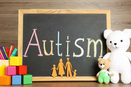 Chalkboard with word Autism, paper cutout of family and different toys on wooden tableの写真素材