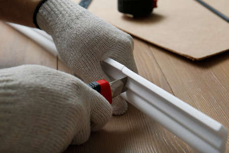 Worker cutting foam crown molding with utility knife at wooden table, closeupの写真素材