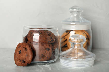 Delicious chocolate chip cookies in glass jars on light gray marble table