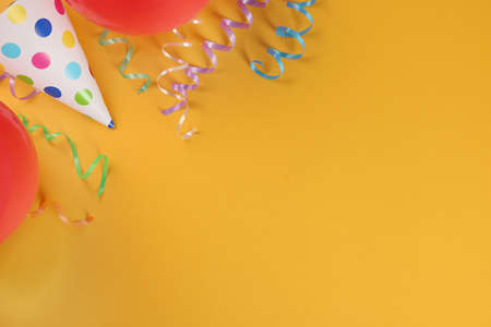 Colorful serpentine streamers, party hat and balloons on orange background, flat lay. Space for textの写真素材