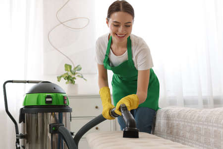 Professional janitor in uniform vacuuming furniture indoorsの写真素材