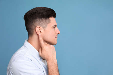 Man pointing at his ear on light blue background. Space for textの写真素材