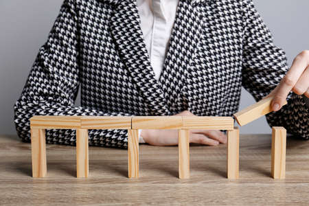 Businesswoman building bridge with wooden blocks at table, closeup. Connection, relationships and...