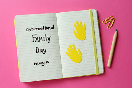Notebook with text International Family Day May 15, pencil and paper clips on pink background, flat layの写真素材