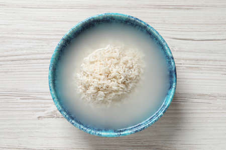 Bowl with rice soaked in water on white wooden table, top viewの写真素材