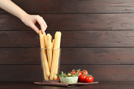 Woman taking fresh delicious grissino from glass at wooden table, closeupの写真素材