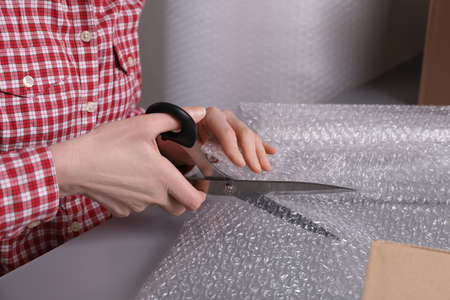 Woman cutting  wrap at table in warehouse, closeup