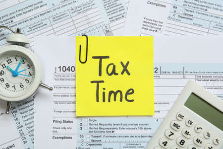 Reminder note with words Tax Time, alarm clock and calculator on documents, flat layの写真素材