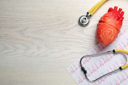 Stethoscope, red heart model and cardiogram on white wooden table, flat lay with space for text....