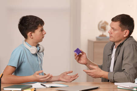 Father talking with his teenage son about contraception while he is doing homework at home. sex...