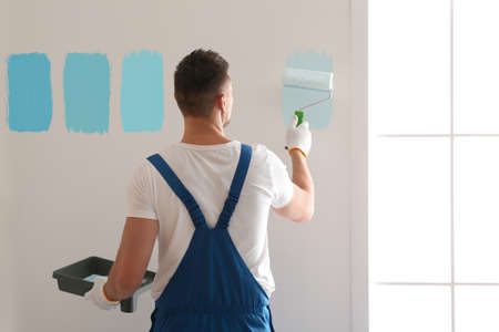 Man painting wall with light blue dye indoors, back viewの写真素材