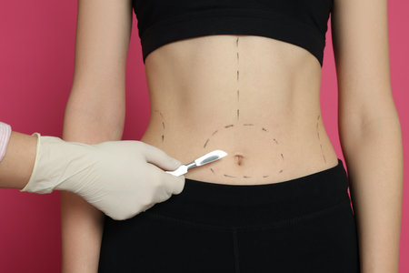 Doctor holding scalpel near slim woman with marks on body against pink background, closeup. weight...