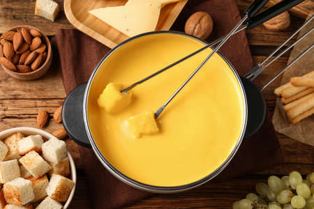 Pot of tasty cheese fondue and snacks on wooden table, flat layの写真素材