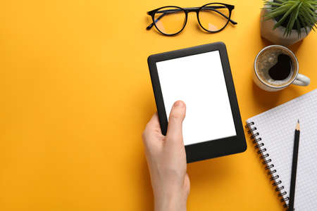 Woman using e-book reader on orange background, top view. Space for text