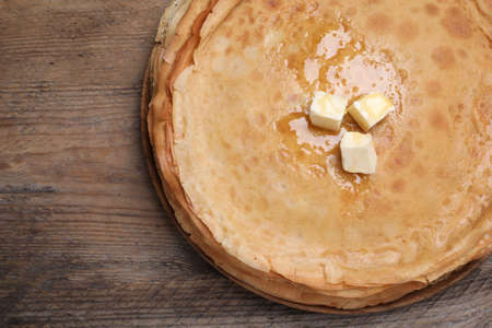 Stack of delicious crepes with melting butter on wooden table, top view