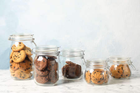 Delicious chocolate chip cookies in glass jars on white marble table