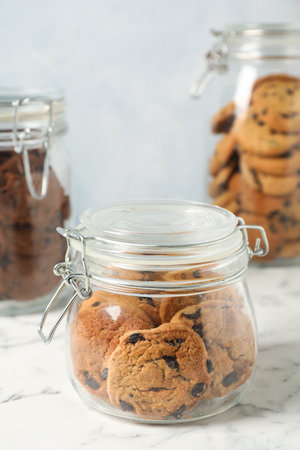 Delicious chocolate chip cookies in glass jars on white marble table