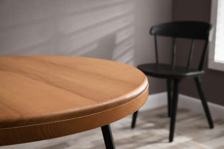 Round wooden table and black chair in room, closeup