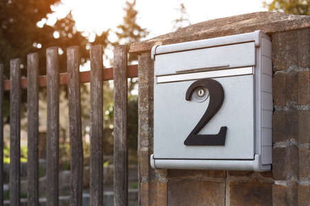Metal mailbox with number 2 on stone fence near wooden gate outdoors, space for textの写真素材