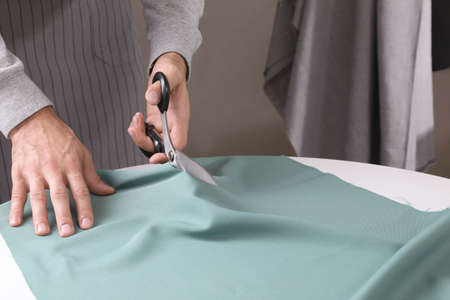 Tailor cutting fabric with scissors at table in atelier, closeupの写真素材