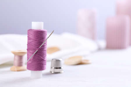Spool of purple sewing thread with needle and thimble on white table, space for textの写真素材