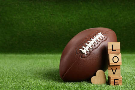 American football ball, cubes with word Love and heart on green grass. Space for textの写真素材