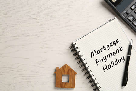Notebook with words Mortgage Payment Holiday, house model and calculator on white wooden table, flat lay. Space for textの写真素材