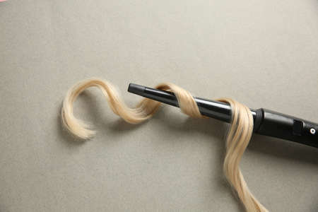 Modern clipless curling iron and blonde hair lock on gray background, top viewの写真素材
