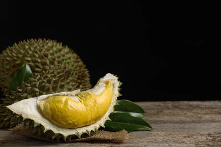 Fresh ripe durian fruits on wooden table against black background, space for text
