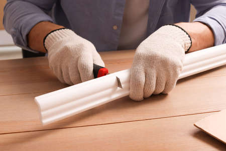 Man cutting foam crown molding with utility knife at wooden table, closeupの写真素材