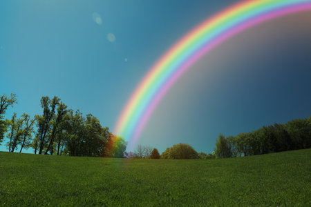 Picturesque view of green meadow and beautiful rainbow in blue sky on sunny dayの写真素材