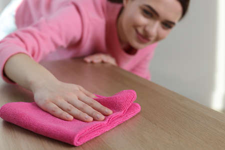 Young woman cleaning wooden table with rag at home, focus on hand. Space for text