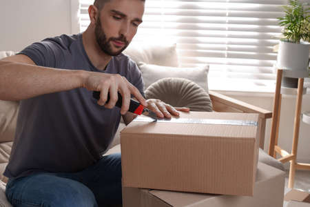 Man using utility knife to open parcel at homeの写真素材