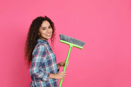 African American woman with green broom on pink background, space for textの写真素材