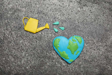 Happy Earth Day. Flat lay composition with plastic planet and watering can on gray table
