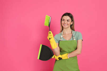 Young woman with broom and dustpan on pink background, space for text