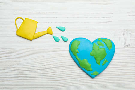 Happy Earth Day. Flat lay composition with plastic planet and watering can on white wooden tableの写真素材