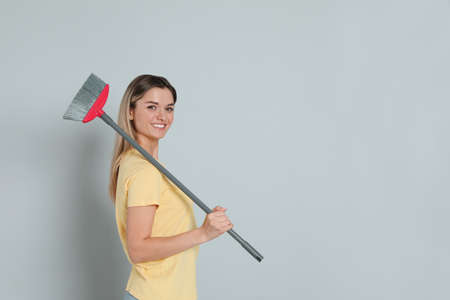 Young woman with broom on gray background, space for textの写真素材