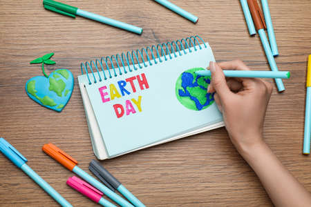 Happy Earth Day. Woman drawing planet in notebook at wooden table, top viewの写真素材