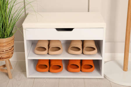 Stylish storage bench with different pairs of rubber slippers and beautiful houseplant near white wall in hallの写真素材