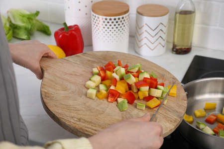 Woman putting cut vegetables into saute pan in kitchen, closeupの写真素材