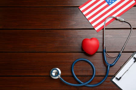 Stethoscope, red heart, clipboard and American flag on wooden table, flat lay. Space for textの写真素材