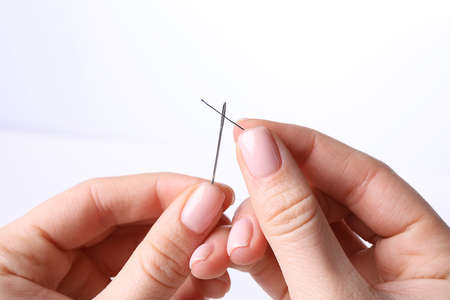 Woman threading sewing needle on white background, closeup